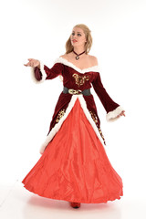 full length portrait of pretty blonde lady wearing red and white christmas inspired costume gown, standing pose on white background. © faestock