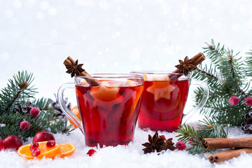 Hot mulled spiced red wine in glass mug with with festive decoration lights and gingerbread . On white snow background