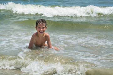 Cute happy baby boy bathes in the sea with waves, vacations
