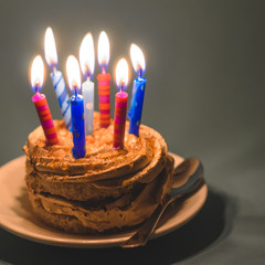 Chocolate cake with cream and lots of burning candles on a dark background.