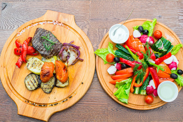Steak with grilled vegetables, and fresh vegetables on a wooden tray