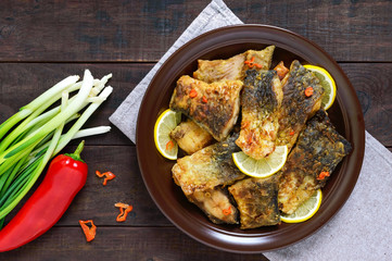 Pieces of fried fish (carp) on a ceramic plate on a dark wooden background. Top view.