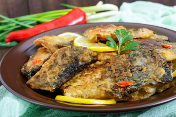Pieces of fried fish (carp) on a ceramic plate on a dark wooden background.
