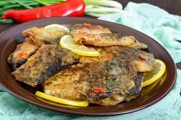 Pieces of fried fish (carp) on a ceramic plate on a dark wooden background.