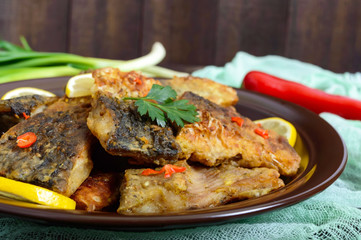 Pieces of fried fish (carp) on a ceramic plate on a dark wooden background.