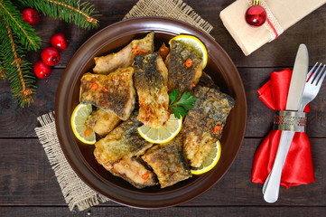 Pieces of fried fish (carp) on a ceramic plate on a dark wooden background. The top view. Christmas menu.