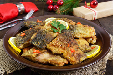 Pieces of fried fish (carp) on a ceramic plate on a dark wooden background.