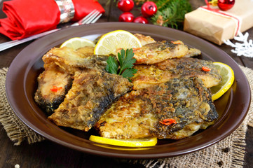 Pieces of fried fish (carp) on a ceramic plate on a dark wooden background.