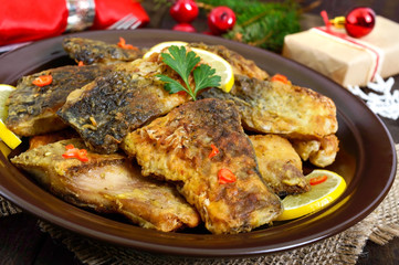 Pieces of fried fish (carp) on a ceramic plate on a dark wooden background.