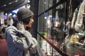 Naklejka na ściany i meble Woman looking her reflection in fashion store showcase in winter night scene