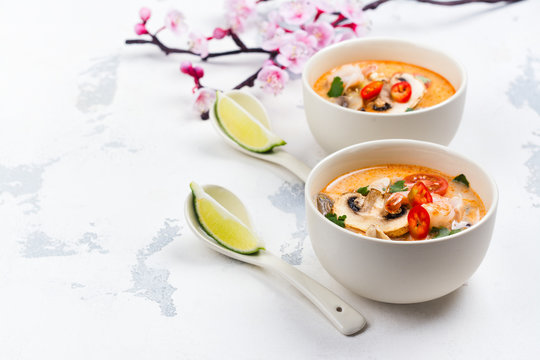 Traditional Tom Yum soup with blooming sakura branch on white stone table