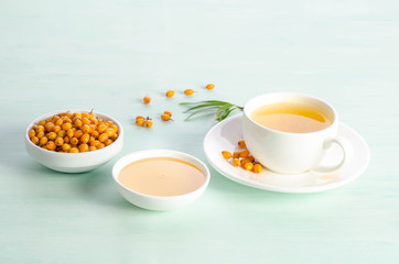 Obraz na płótnie Canvas Sea buckthorn in porcelain bowl, honey and cup of tea with Sea buckthorn on blue table. top view