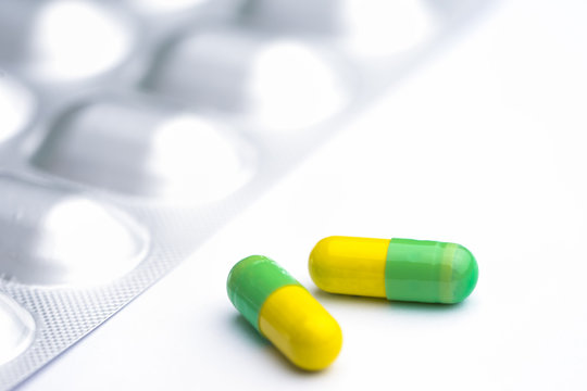 Green and yellow capsules on white background. Two medication pills with foil pack.