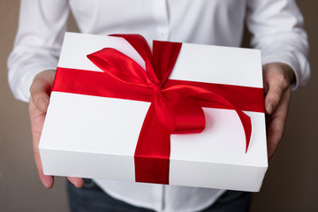 A woman in a white shirt gives a gift. White box with red satin bow with tablet inside. Cropped...