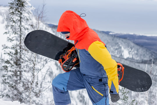freerider with a snowboard in overalls stands on top of a snowy mountain