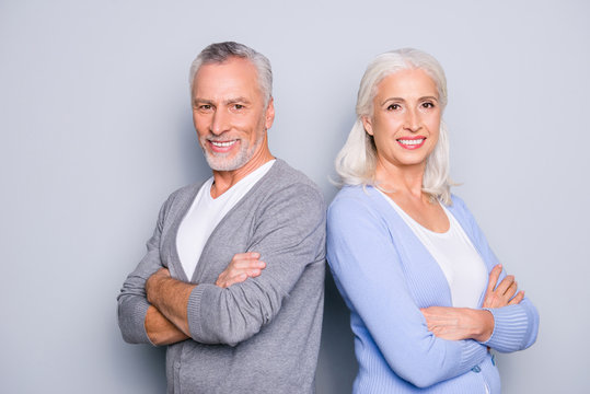 Concept of being good workers even when you are aged person. Two confident elderly people standing with crossed arms back to back against grey background