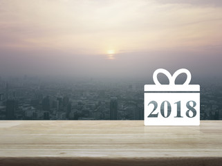 Gift box happy new year 2018 icon on wooden table over aerial view of cityscape at sunset, vintage style