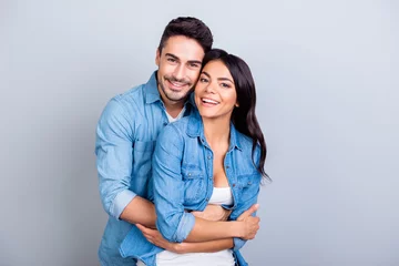 Fotobehang Portrait of cheerful lovely cute couple with beaming smiles hugging and looking at camera over grey background © deagreez