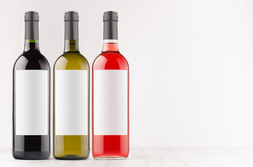 Wine bottles collection - red, green, black- with blank white labels on white wooden board, mock up, copy space. Template for advertising, design, branding identity.