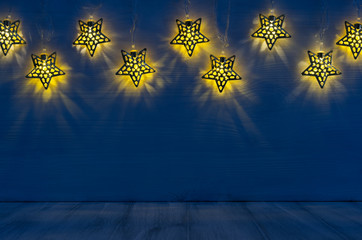 Christmas decor - lights shaped stars glow on indigo blue wooden background.