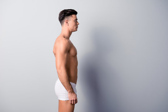 Side view photo of handsome condifend guy wearing white underwear and staying still against grey background