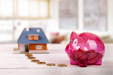 conceptual shot with piggy bank and house scale model on the table in the room