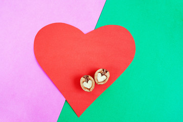 Red paper heart and two walnut in shape of heart on it on lilac-green background.