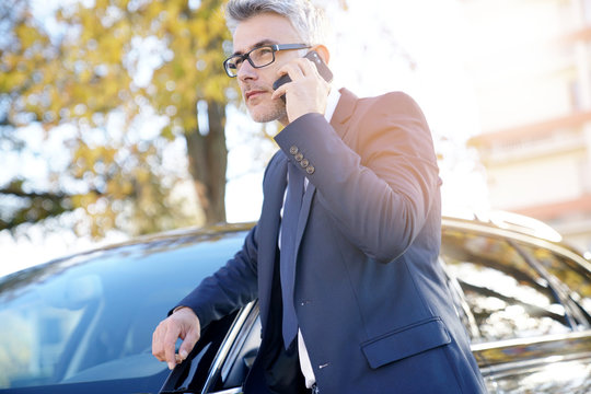 Businessman talking on phone standing outside the car