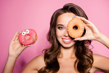 Funny adorable charming girl with beaming smile holding tasty donut near eye, fooling around....