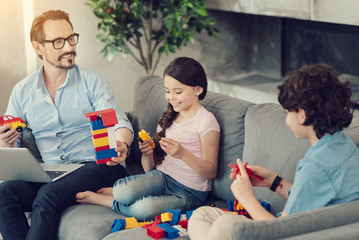 Family entertainment. Joyful positive happy family sitting together on the sofa and playing with construction set while having fun
