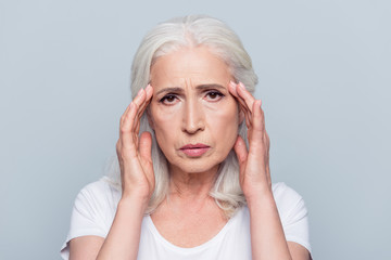 Upset, sad, pretty, nice, attractive woman having head ache, stress, troubles, touching temples with fingers, looking at camera, standing over grey background