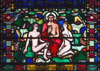 LONDON, GREAT BRITAIN - SEPTEMBER 16, 2017: The Adam and Eva in paradies with the Jesus on the stained glass in church St Etheldreda by Charles Blakeman (1953 - 1953).