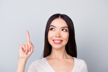 Successful, pretty, smiling  woman  on grey background  is pointing up  with her fingers