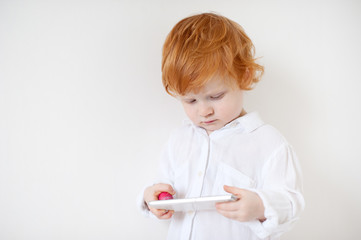 Red-haired boy in a white shirt looks at the phone