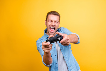 Portrait of young, cheerful, attractive, very excited guy holding joystick and playing video games over yellow background