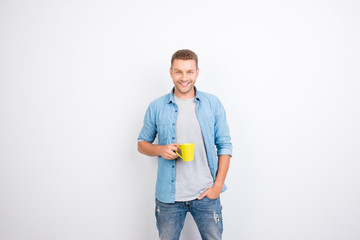 Portrait of cheerful, peppy guy holding yellow mug with coffee and one hand in pocket, getting a charge of vivacity, looking at camera, standing over white background