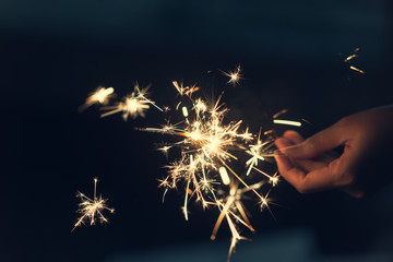 Female hands holding sparkler with night background - bright festive Christmas or New Year’s Eve