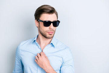 Portrait of cool, elegant man in black spectacles holding hand on button of shirt, looking to the side over grey background