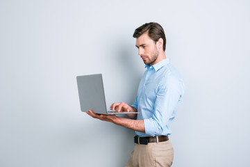 Portrait of attractive, successful, concentrated, attractive secretary in shirt, holding laptop, looking at screen, using wifi for work, developing new project, start up over grey background