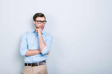 Portrait with copy space of attractive, clever, stunning man in shirt, pants and glasses touching chin with hand looking to the side with thoughtful expression over grey background