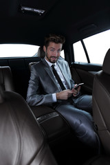 Fototapeta na wymiar man in suit sitting in car and reading messages on smartphone