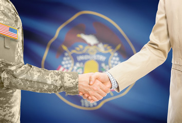 USA military man in uniform and civil man in suit shaking hands with certain USA state flag on...