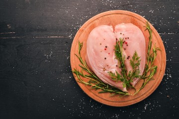 Raw chicken breast fillet with rosemary and spices on a black wooden background. Top view. Free space for text.