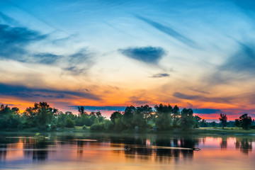 Naklejka premium Sunset above river with green forest on the other coast and reflection on water