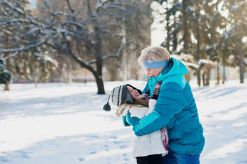 
Active atractive grandmother in sporty jacket and her granddaughter play together in winter city park