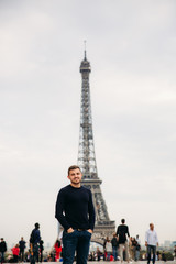 Fototapeta na wymiar A young man wearing a dark blue jacket is standing on the background of the Eiffel Tower. Sunny weather is autumn