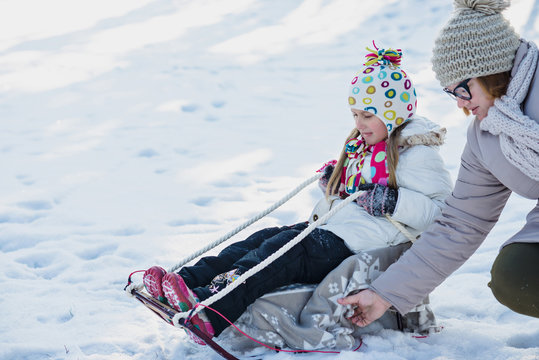Mother and daughter sledging in winter park