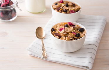 Bowl of homemade muesli with nuts, berries, dried fruits, milk on white wooden background. Healthy breakfast. 