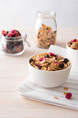 Bowl of homemade muesli with nuts, berries, dried fruits, milk on white wooden background. Healthy breakfast. 