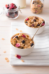 Bowl of homemade muesli with nuts, berries, dried fruits, milk on white wooden background. Healthy breakfast. 